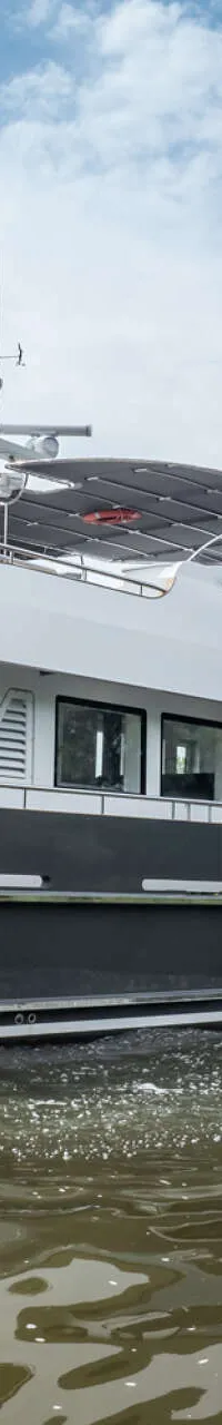Een donkergrijze motorboot met witte opbouw vaart op een rivier onder een bewolkte hemel. — Bloemsma Trawler 70