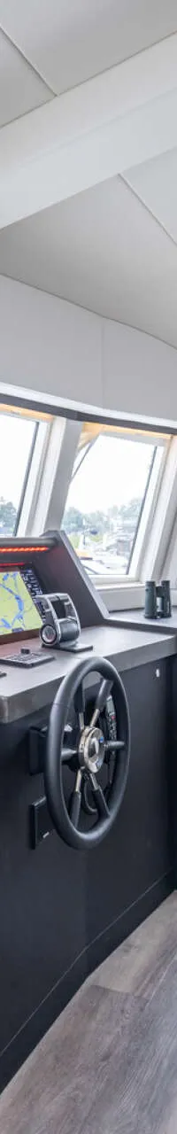 De foto toont het interieur van een stuurhut met een stuurstand, een kapiteinsstoel en diverse navigatieschermen.