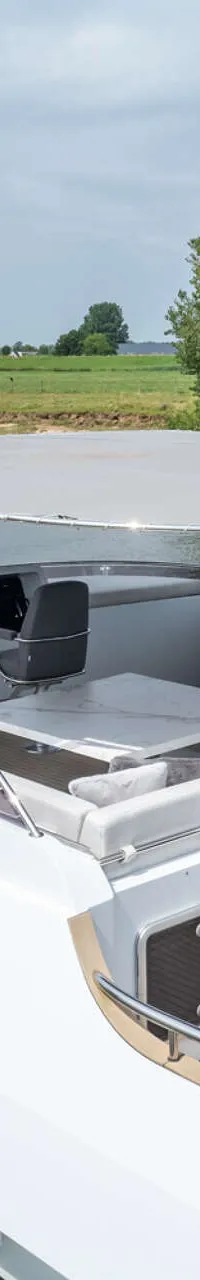 Een witte motorboot vaart op een rivier met groene oevers, met een bijboot en een Nederlandse vlag achterop.