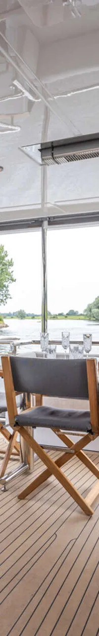 Een teakhouten dek met een eettafel en stoelen aan boord van een boot, met uitzicht op een waterweg. — Bloemsma Trawler 70