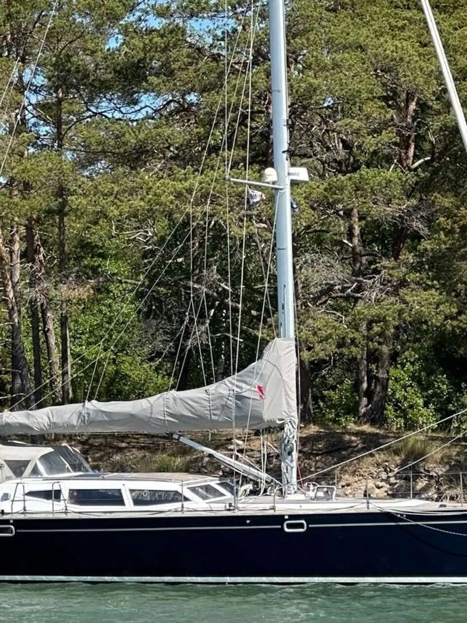 Een donkerblauwe zeilboot met een witte opbouw en opgerolde zeilen ligt aangemeerd aan een houten steiger. — Nordbaelt 50