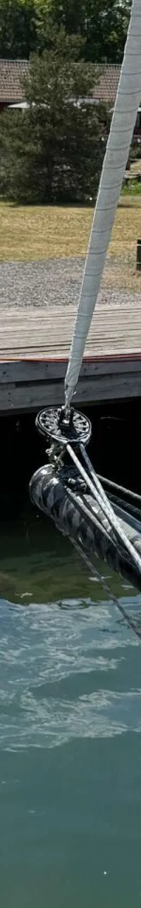 De foto toont het teakhouten dek van een zeilboot met twee stuurwielen, lieren en een buitenboordmotor aan de spiegel.