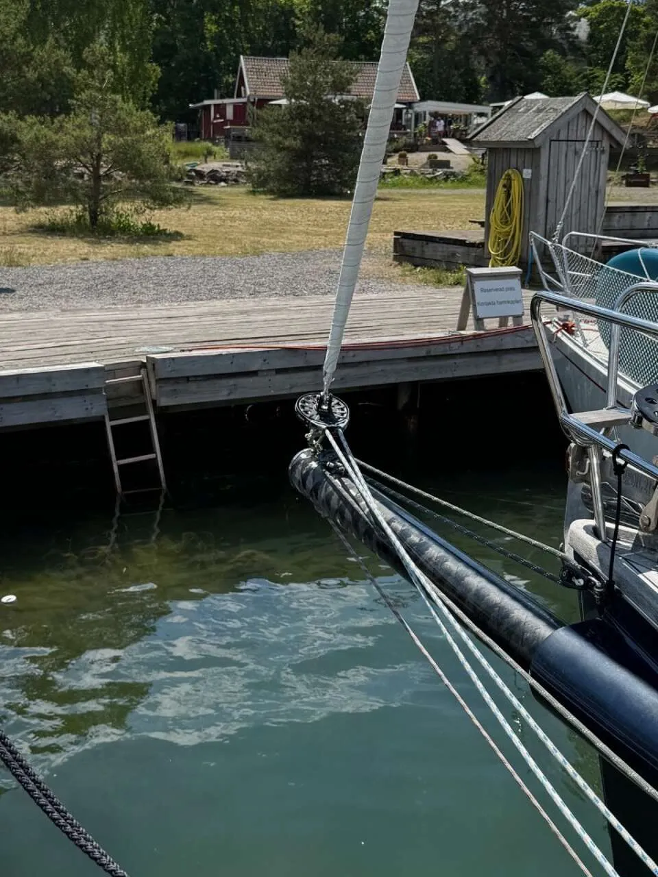 De foto toont het teakhouten dek van een zeilboot met twee stuurwielen, lieren en een buitenboordmotor aan de spiegel.