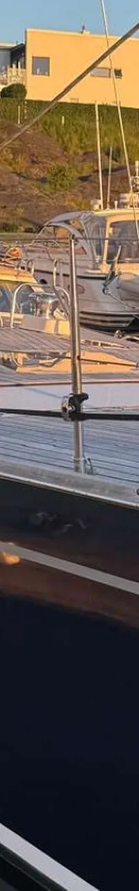 Een bovenaanzicht van het teakhouten dek van een zeilboot met luiken, lieren en een mast, naast een andere boot.