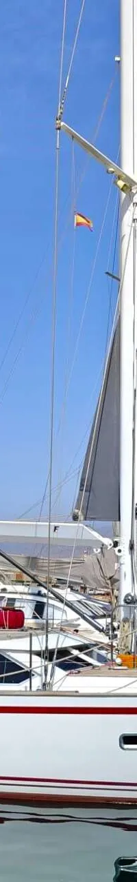 Een witte zeilboot met rode strepen ligt in een haven, met een stad en bergen op de achtergrond. — Premier Dixon  62