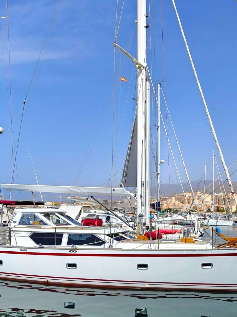 Een witte zeilboot met rode strepen ligt in een haven, met een stad en bergen op de achtergrond. — Premier Dixon  62