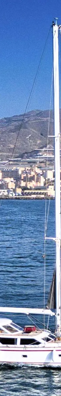 Een witte zeilboot met twee masten vaart op blauw water voor een kustlijn met bebouwing en bergen. — Premier Dixon  62