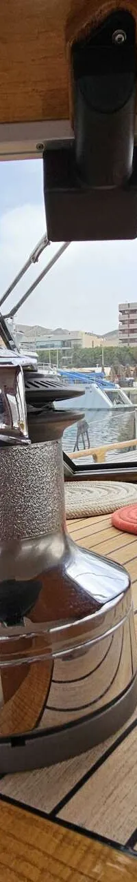 Een interieurzicht van een boot met houten afwerking, een lier, en uitzicht op een haven met andere boten en gebouwen.