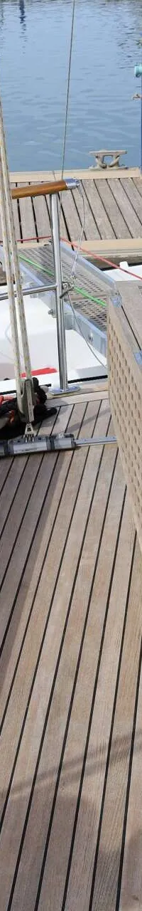 De foto toont het teakhouten dek van een zeilboot met twee houten banken, een tafel en een buitenboordmotor.