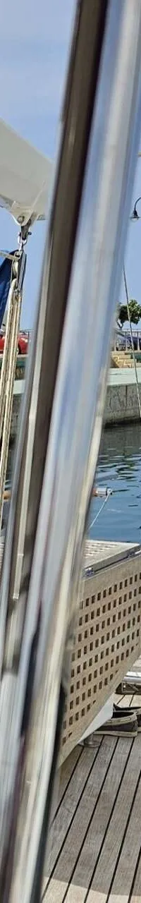 Een dek van een zeilboot met houten planken, relingen en een rode kussen, met een jachthaven op de achtergrond.