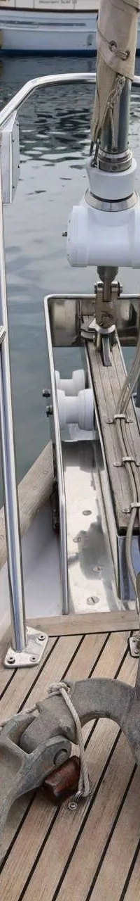 De foto toont de boeg van een zeilboot met een anker, ankerketting, touwen en een reling, liggend in het water.