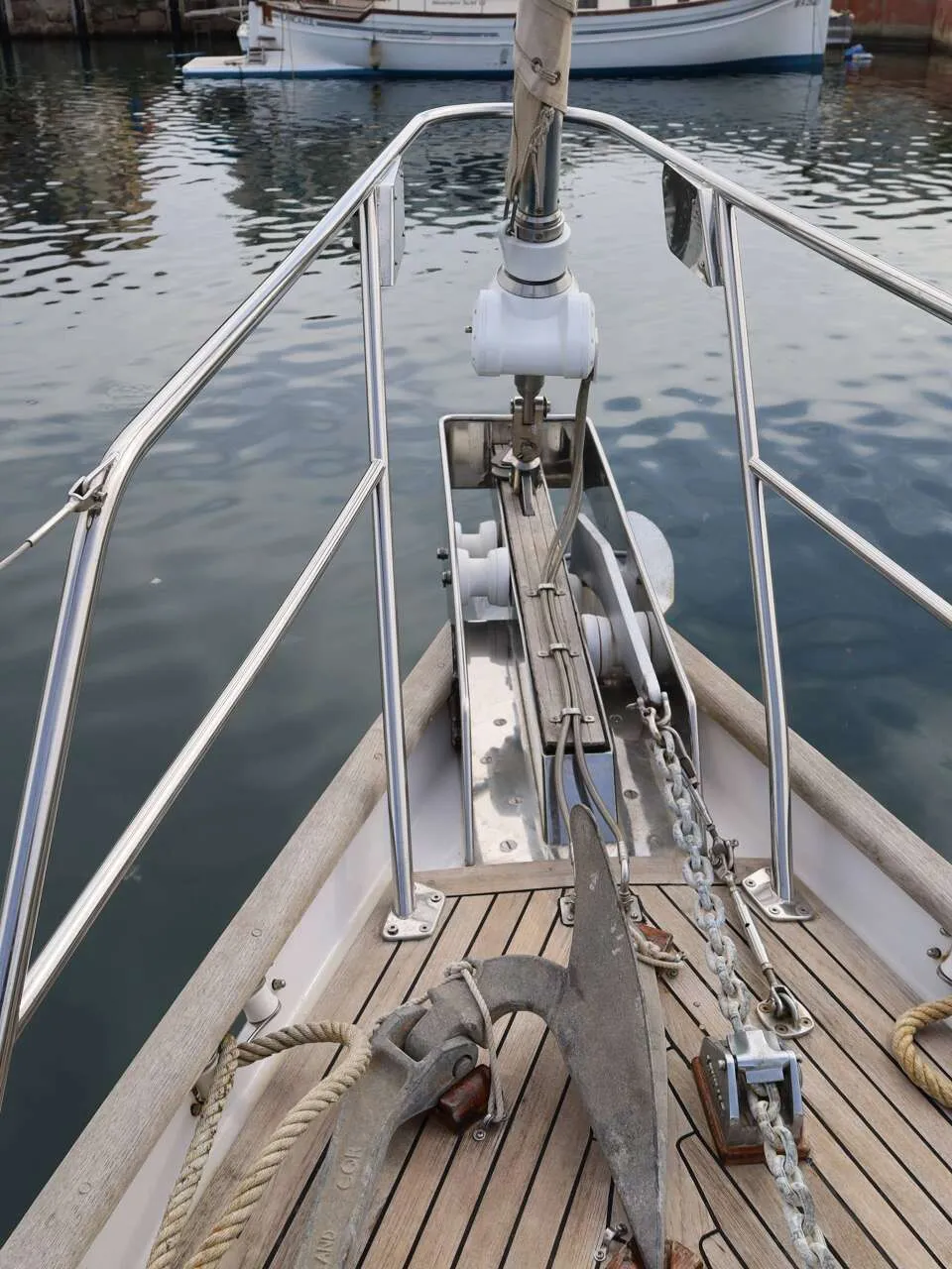 De foto toont de boeg van een zeilboot met een anker, ankerketting, touwen en een reling, liggend in het water.
