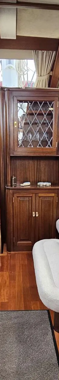 De foto toont een houten interieur van een boot met zitbanken, een tafel, kussens, ramen en een kast. — Premier Dixon  62