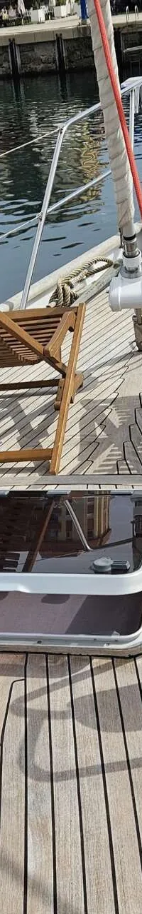 Een houten dek van een boot met twee ligstoelen, luiken, lieren en een reling, liggend in een haven. — Premier Dixon  62