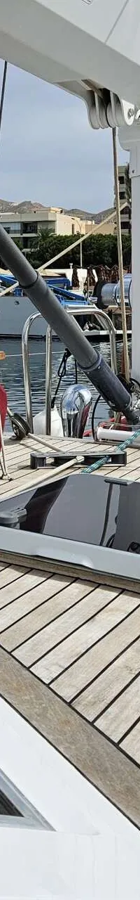 Een teakdek met een luik, een opgerold touw onder een raam, en een rode hoes met een tafelblad erop.