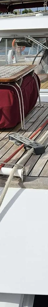 Een dek van een boot met houten planken, een witte opbouw met ramen, en een rode hoes over een tafel. — Premier Dixon  62