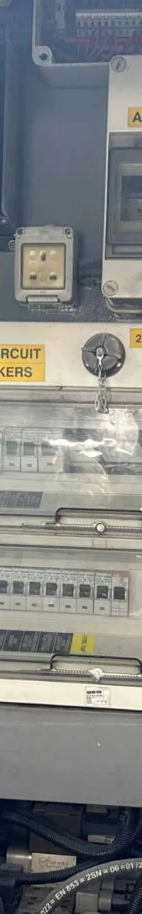 De foto toont een deel van een elektrisch paneel met diverse schakelaars, zekeringkasten en een acculader.