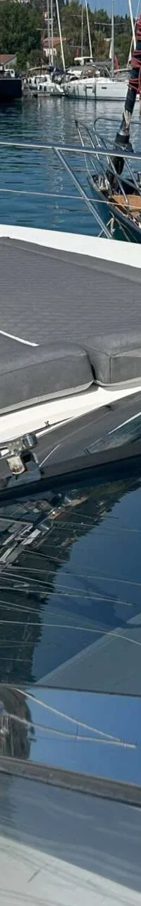 De foto toont het voordek van een witte boot met grijze kussens en een voorruit, met andere boten in de achtergrond.