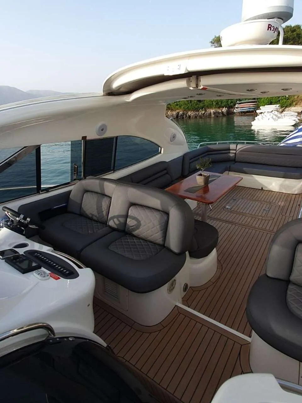Een jacht met een stuurstand, zitplaatsen, een tafel en een Griekse vlag, liggend aan een steiger. — Sunseeker Predator 56