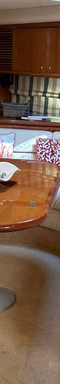 Een interieur van een boot met een U-vormige crèmekleurige bank, een houten tafel en kasten, en een doorgang naar een…