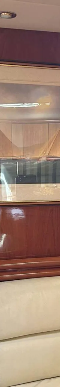 Een interieur van een boot met een crèmekleurige bank, houten wanden, een schilderij van zeilboten en een open deur naar…
