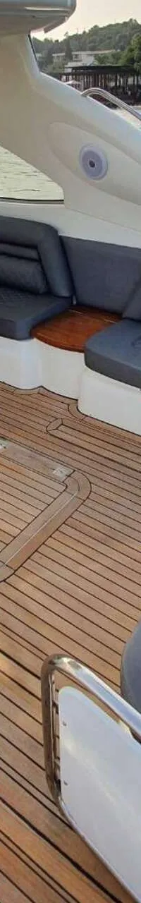 Een luxe jacht met een teakhouten dek, een grijze L-vormige bank en een houten tafel met een plantje. — Sunseeker Predator 56