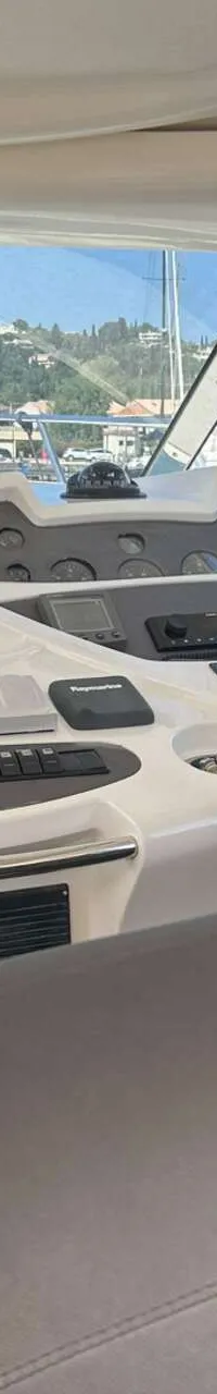 De foto toont het stuurhuis van een boot met een stuurwiel, instrumentenpaneel en een Raymarine-scherm.