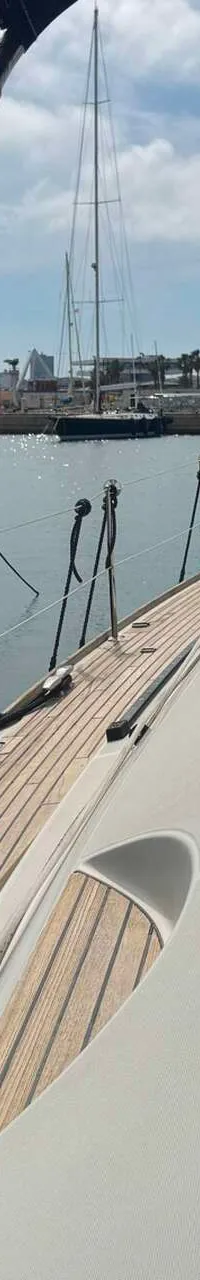 Een zeilboot met teakhouten dek ligt aangemeerd naast een grotere motorboot in een haven. — Jeanneau Sun Odyssey 54 DS