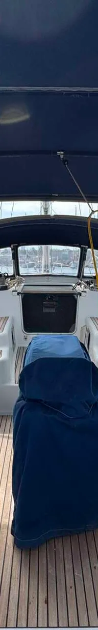 Een bovenaanzicht van de kuip van een zeilboot met een blauwe buiskap, teakhouten dek en twee stuurwielen met blauwe hoezen.
