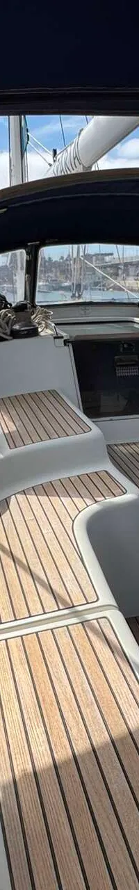 Een bovenaanzicht van de cockpit van een zeilboot met teakhouten dek, blauwe buiskap en een afgedekt stuur.
