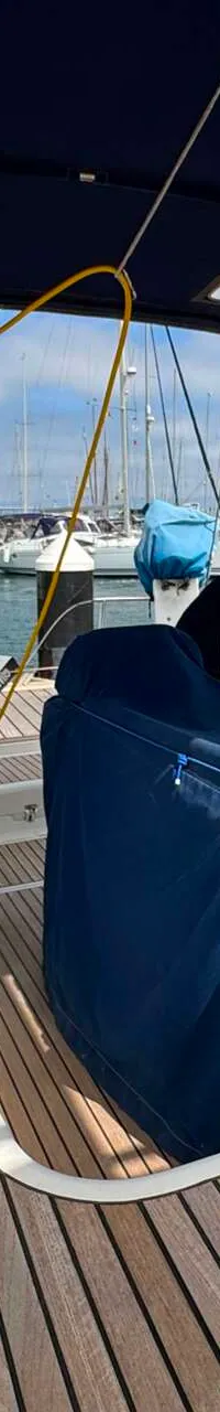 De kuip van een zeilboot met teakhouten dek, twee stuurwielen en een blauwe afdekhoes over de stuurstand.