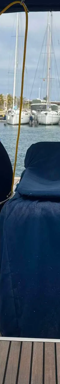 Een achterdek van een zeilboot met teakhouten vloer, twee stuurwielen met blauwe hoezen en een blauwe hoes over de…