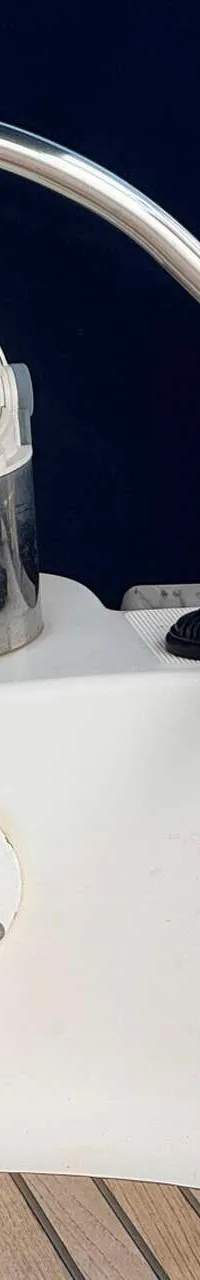Een detailfoto van een bootdek met een lier, touwen, een bekerhouder en een wit navigatielicht.
