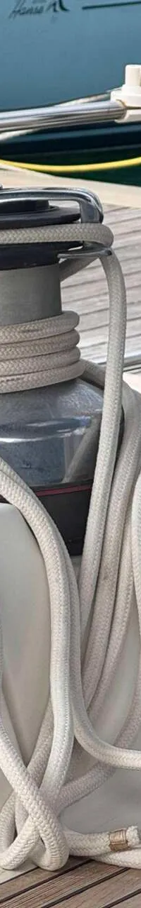 Een lier met touw, een witte helm op een metalen pot, en een blauwe hoes zijn zichtbaar op een boot.