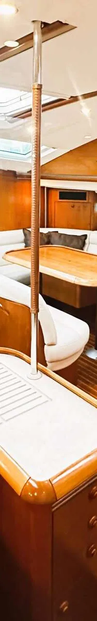De foto toont het interieur van een boot met houten vloeren en wanden, witte banken, een tafel en een kombuis.