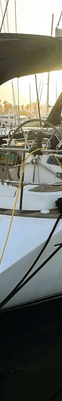 Een witte zeilboot met de naam "SPARTIA" en "SUN ODYSSEY 54 DS" ligt afgemeerd in een haven, met een zwarte bimini.