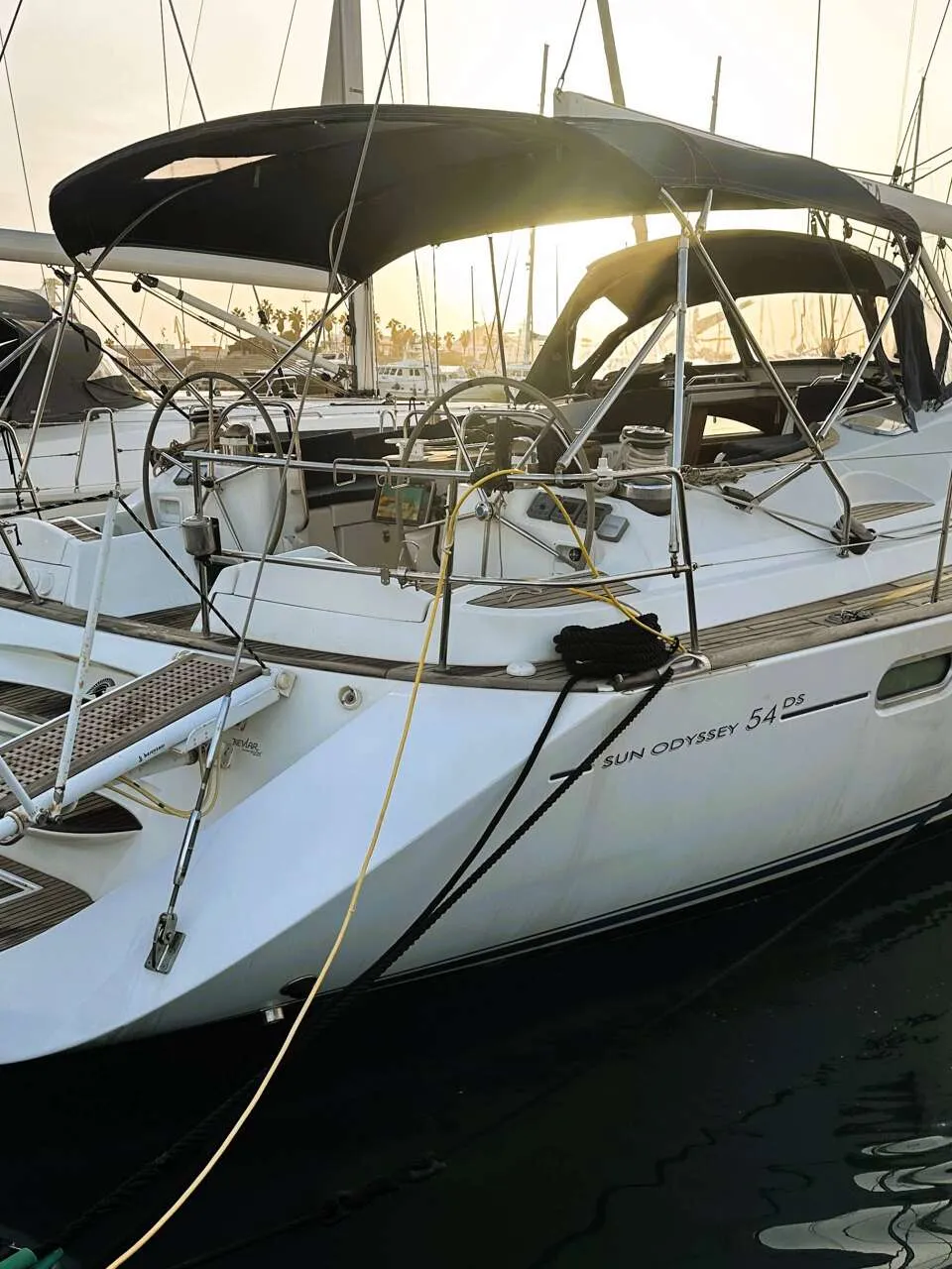 Een witte zeilboot met de naam "SPARTIA" en "SUN ODYSSEY 54 DS" ligt afgemeerd in een haven, met een zwarte bimini.