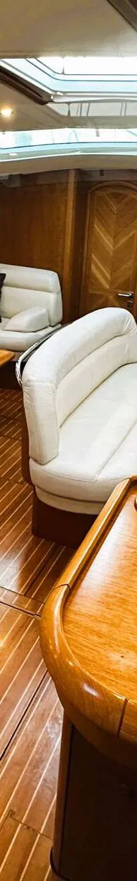 De foto toont het interieur van een boot met houten vloeren en wanden, witte banken, tafels en een kombuis.