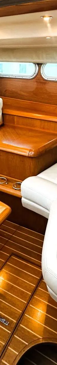 De foto toont een interieur van een boot met twee witte banken, een houten tafel, een houten vloer en houten wanden.
