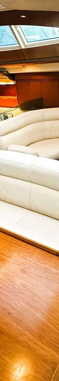 De foto toont het interieur van een boot met een houten tafel, witte banken, een kombuis en een trap naar het dek.