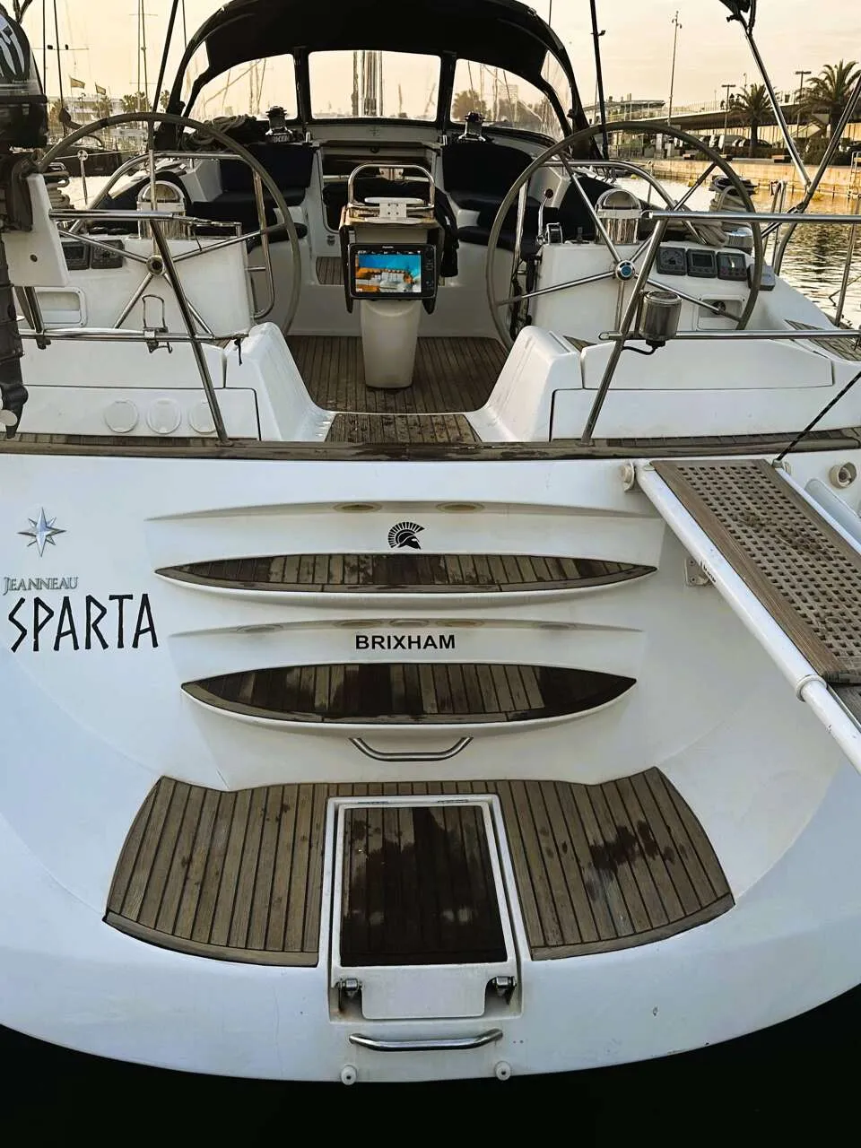 De achterkant van een witte zeilboot met de naam "SPARTA" en "BRIXHAM" is zichtbaar, inclusief een Yamaha buitenboordmotor…
