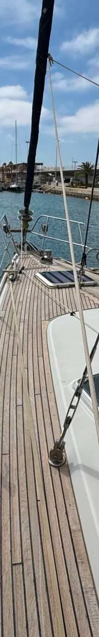 Vanaf de boeg van een zeilboot is een houten dek met luiken te zien, uitkijkend over een jachthaven met andere boten.