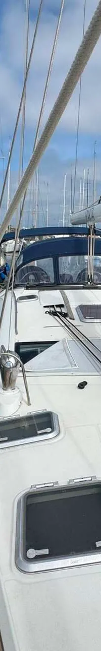 Een wit zeiljacht met een teakhouten dek ligt afgemeerd in een jachthaven, met een mast en diverse luiken zichtbaar.