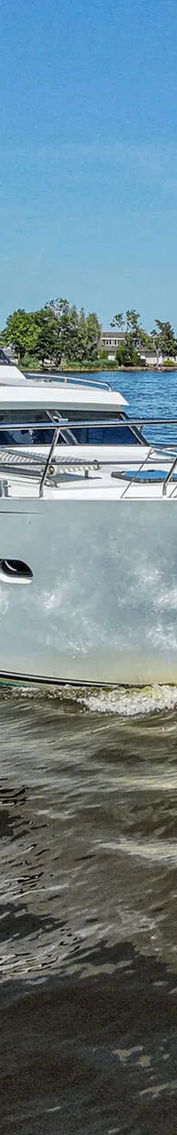 Een witte motorjacht vaart op het water met een blauwe lucht en groene oevers op de achtergrond.