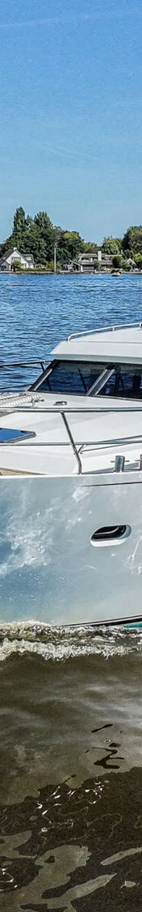 Een witte motorjacht met de naam "Harmony" vaart op blauw water onder een heldere hemel, met land in de achtergrond.