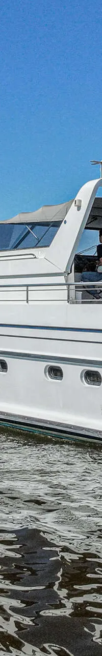 Een witte motorjacht met de naam "Harmony" vaart op het water, met een persoon aan het roer.