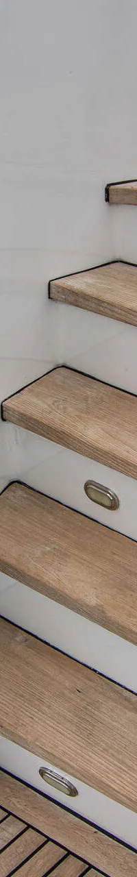Een witte trap met houten treden en ingebouwde verlichting leidt omhoog vanaf een teakhouten dek, met donker water ernaast.