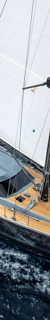 Een zeilboot met witte zeilen en een donkere romp vaart op open water, met een vlag aan de achtersteven.