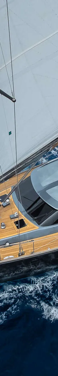 Een zeilboot met twee witte zeilen en een teakhouten dek vaart op open water met vier personen aan boord.
