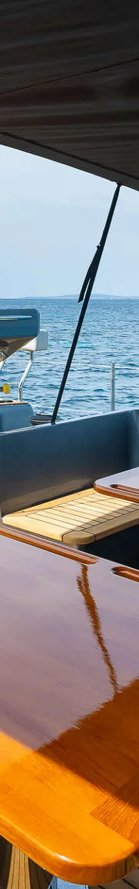 Een teakdek met twee glanzende houten tafels, twee stuurwielen en een donkergrijze bimini met het logo "DE VALK YACHT…